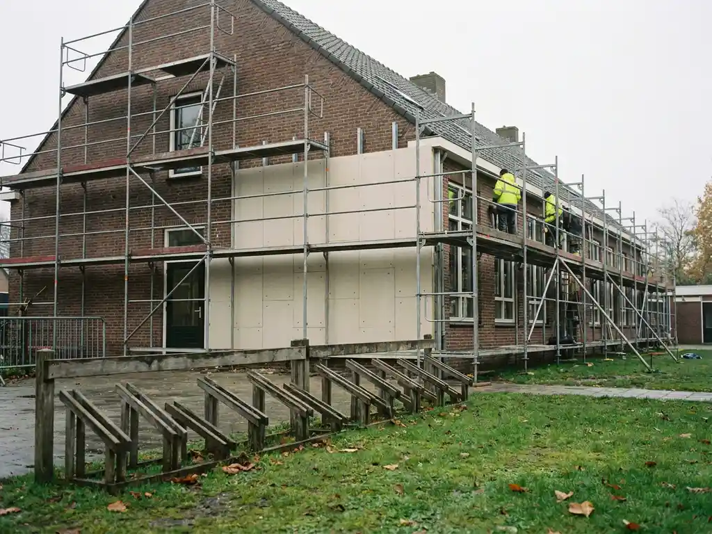 Nederlandstalige basisschool met steigers en isolatiepanelen tijdens renovatie, fietsenrek en groen schoolplein op voorgrond.