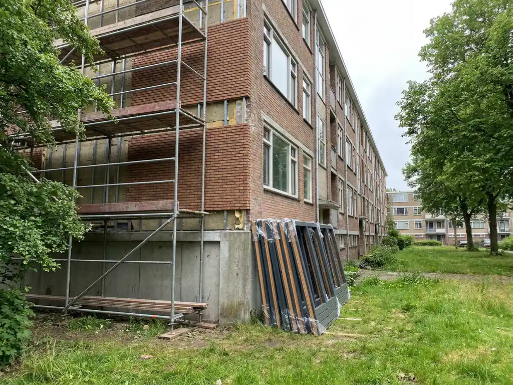 Sociale huurwoning in renovatie met nieuw geïsoleerd metselwerk, gestapelde kozijnen en steigers in bewolkt Nederlands daglicht.